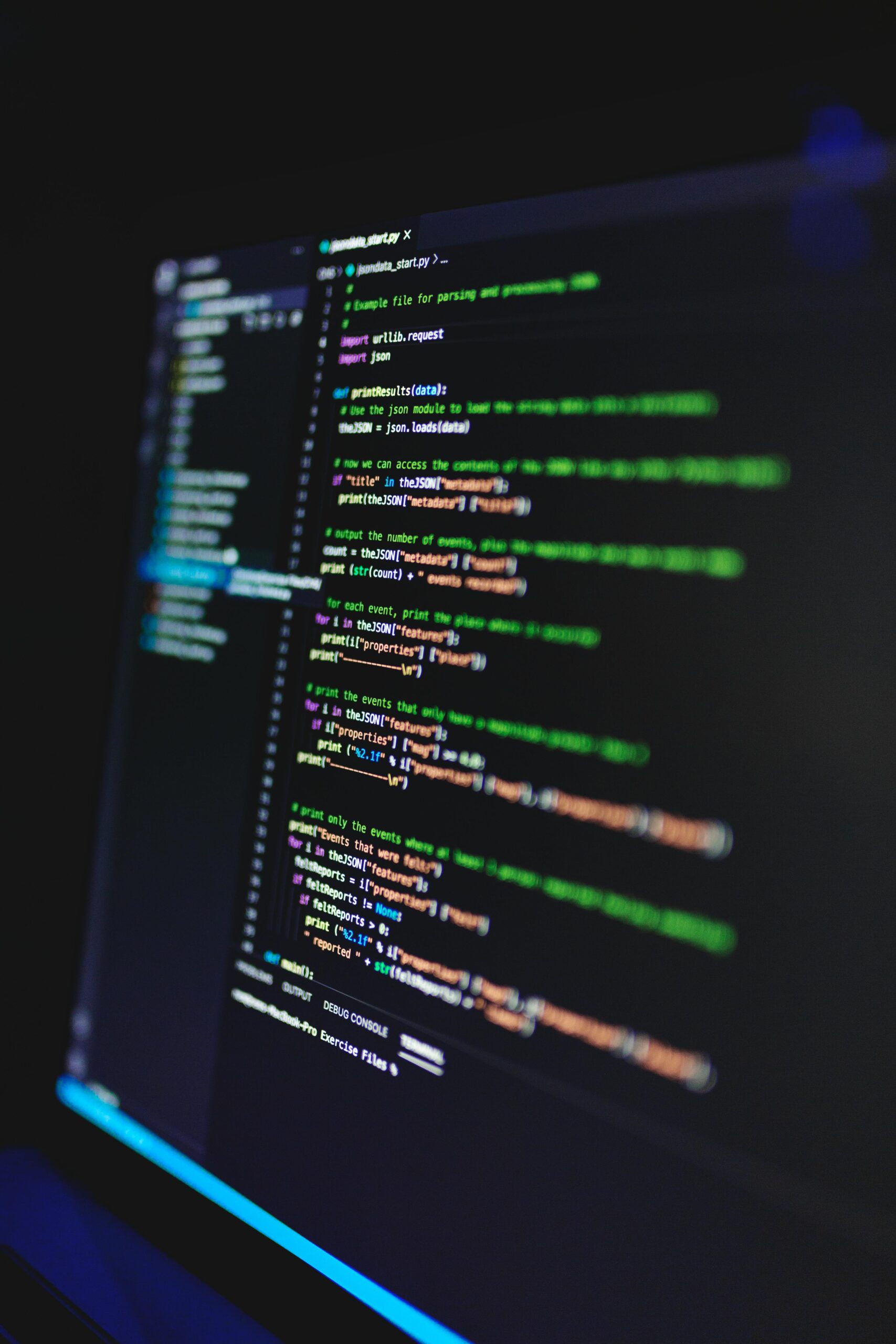 Vertical shot of colorful programming code on a screen in a dark room, highlighting technology work.
